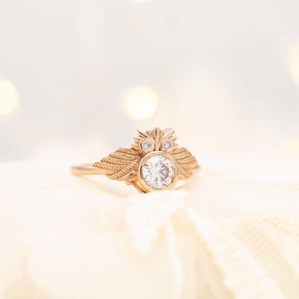 An owl-lover's engagement ring with a round diamond center stone surrounded by an intricately carved owl in rose gold.