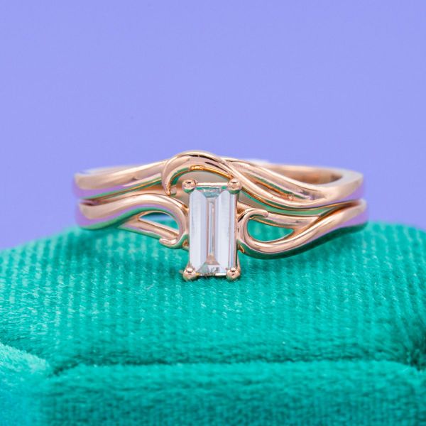 Sweeping lines of rose gold surround this bridal set’s baguette cut diamond.