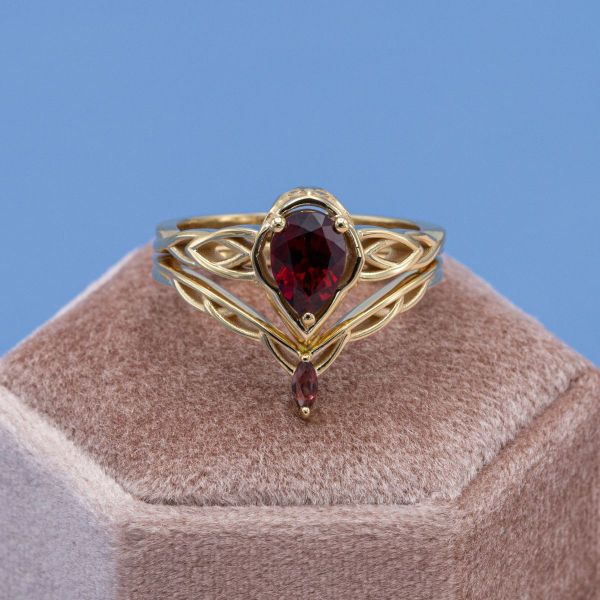 A red spinel sits on a yellow gold band in this fantasy-inspired bridal set that features a matching drop accent stone.