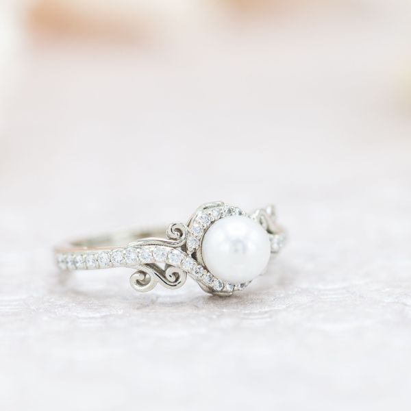 珍珠和钻石镶嵌在戒指上，沿着戒指的肩部镶嵌着优雅的白金曲线。