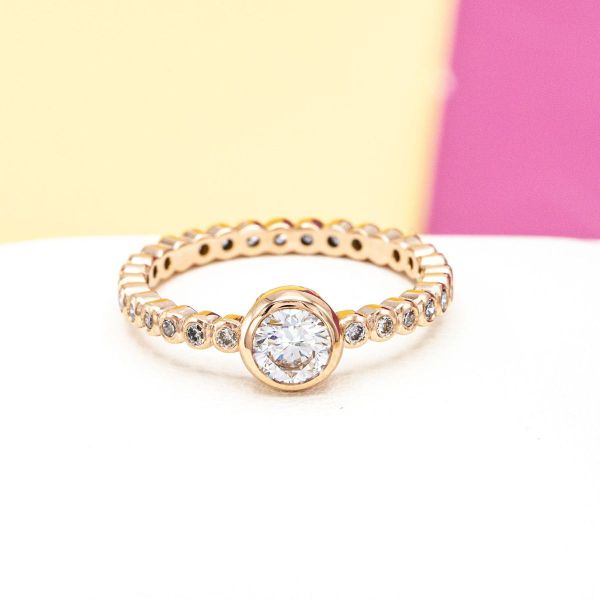 The pavé-set diamonds and center diamond of this engagement ring are wrapped in rose gold circles for a scalloped look.