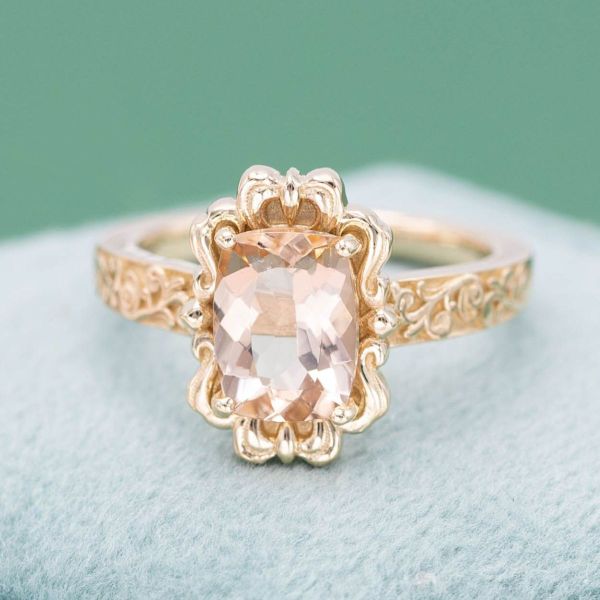 A stunning morganite stone is set in a vintage style frame with an elaborately decorated band.