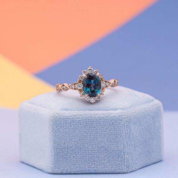 A blue alexandrite is surrounded by diamond accents in a vintage inspired engagement ring.