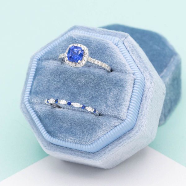 Sapphires take center stage in this white gold bridal set! A cushion cut light blue sapphire sits in the center of the engagement ring, surrounded by a halo and pavé of diamond accents. To match, we've designed a wedding band featuring marquise cut lab diamonds and even more blue sapphires.