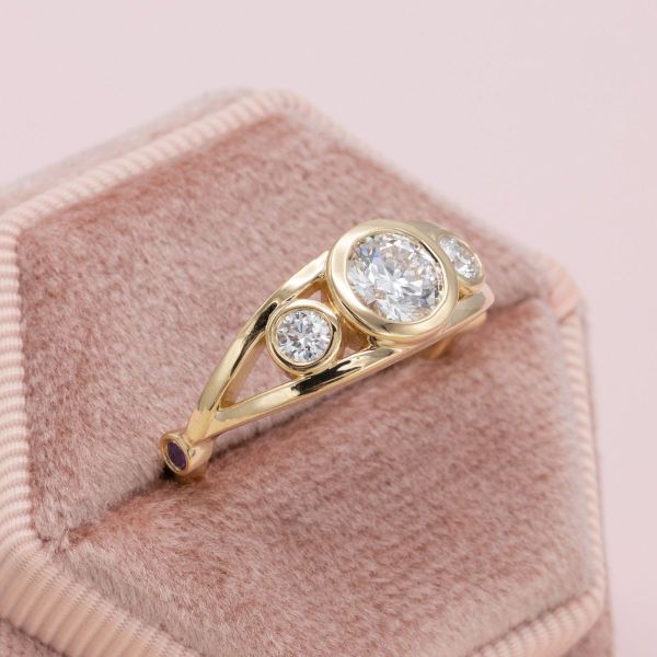 A bezel-set center diamond and diamond side stones sit on a yellow gold band.