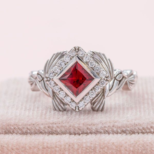 A lab created ruby in a princess cut sits in the center of this hummingbird engagement ring