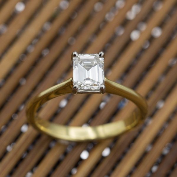 An elegant solitaire setting for a bright emerald cut diamond, creating subtle contrast between the geometry of the stone and the curve of the band.