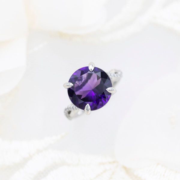 A brilliant round amethyst sits in the center of a platinum engagement ring.