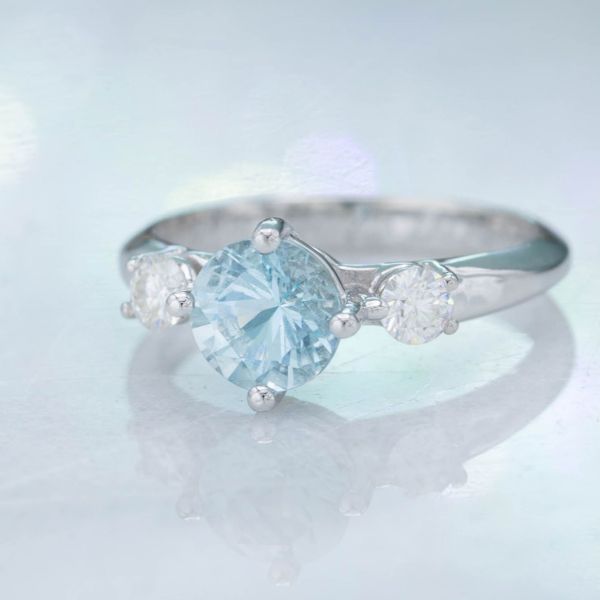 A clean, modern three stone arrangement, flanking the aqua center stone with moissanite side stones.