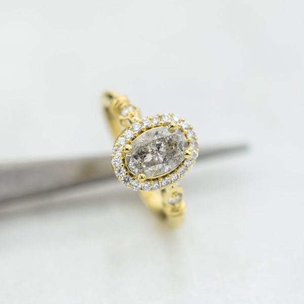 A salt and pepper diamond is held by yellow gold and a halo of white diamonds.