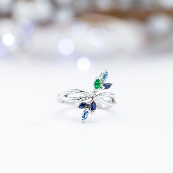 This non-traditional engagement ring uses bold, sweeping curves and delicate clusters of sapphire, aquamarine and emerald in place of a center stone.