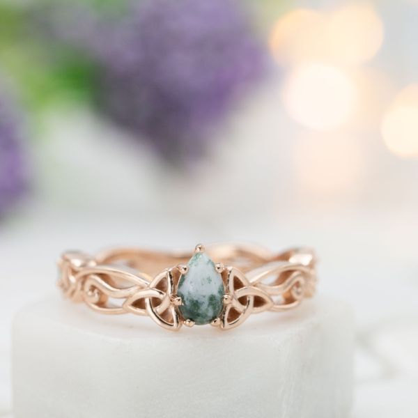 Curvy rose gold engagement ring with Celtic knots and a pear cut moss agate center stone.