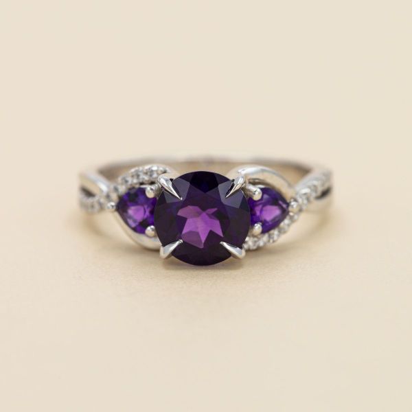 Purple is the name of the game for this engagement ring, featuring an amethyst center stone flanked by amethyst side stones and a spattering of diamond accents.