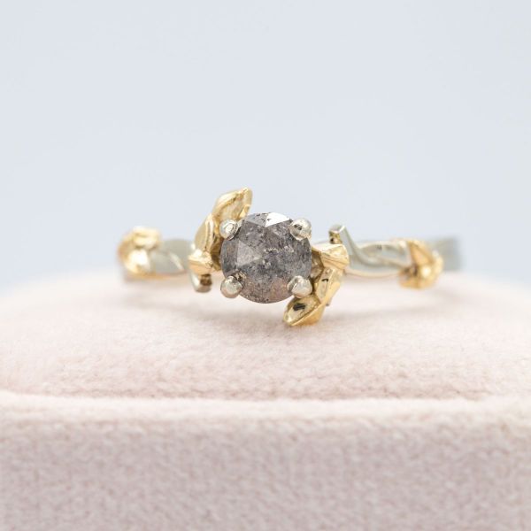 A salt and pepper diamond in a rose cut sits in a mixed yellow and white gold band.