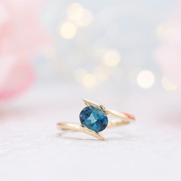 This ring's gold bypass band creates a faux-tension setting for the blue tourmaline center stone.