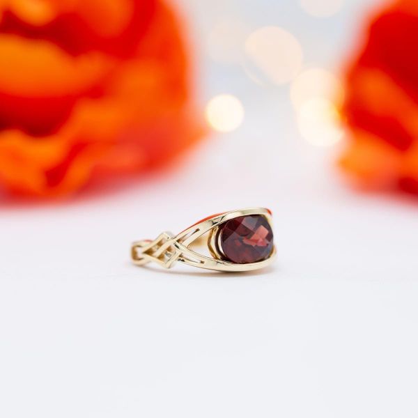 Oval checkerboard faceted red garnet in an east-west setting with a half-bezel gold setting.