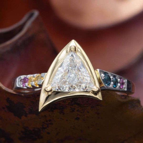 A bold trillion cut diamond rests in the center of a Star Trek inspired engagement ring, surrounded by shimmering gemstone