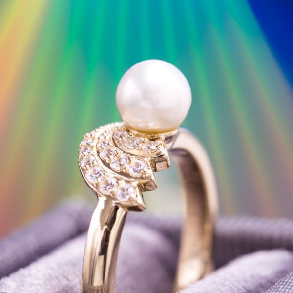 This gold ring sets three diamond comet trails curving away behind the white pearl center stone.
