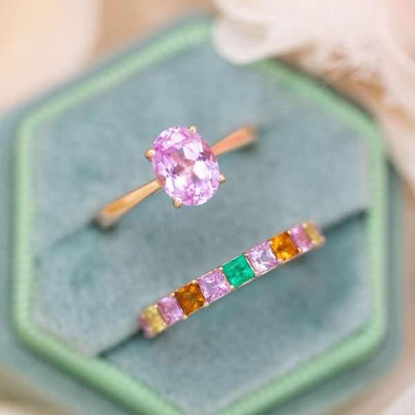 Pretty in pink is the name of the game with this colorful bridal set featuring a lab-created, light pink sapphire in an oval cut at the center of the rose gold, solitaire engagement ring. Matching pink sapphires, orange citrines, light green peridots, and a lush green emerald line the rose gold wedding band for a colorful take on a classic style.