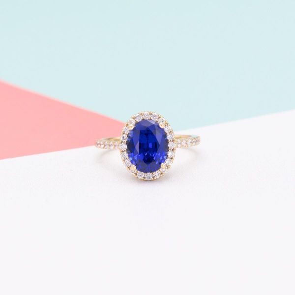A lab created blue sapphire is front and center in a halo of diamonds on this yellow gold engagement ring.