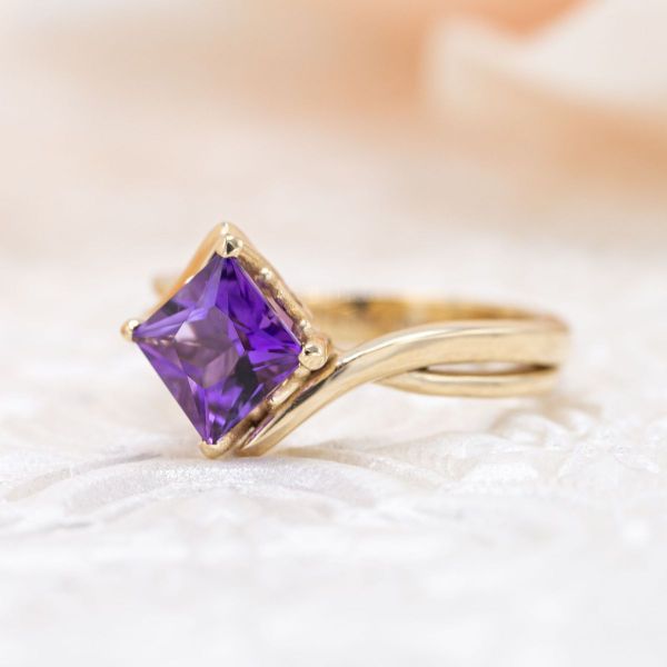 A princess cut amethyst shines a deep purple in this yellow gold engagement ring