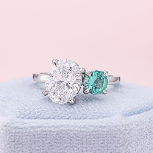 The oval diamond gently leans into a mint-green emerald in this toi-et-moi engagement ring.