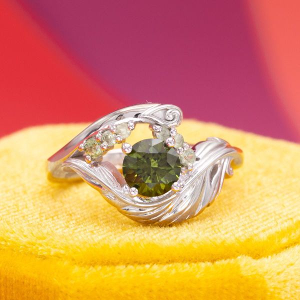 This white gold band features a feathery theme and a green sapphire center stone and accents.