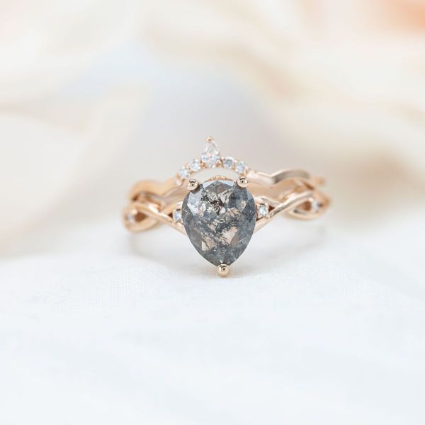 The salt and pepper diamond in the center of this engagement ring has many dark gray inclusions veining through it.