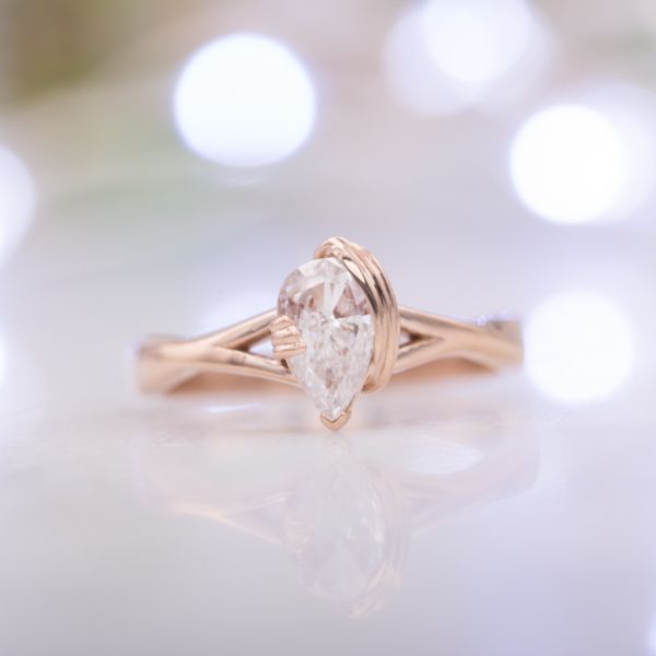 一款精致的玫瑰金戒指，带有雕塑般的扭曲感(双关语):三股项链环绕着梨形切割的钻石。