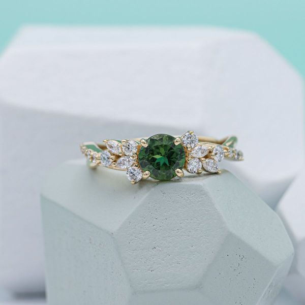 Round green sapphire in a yellow gold floral band with marquise cut diamond accents.